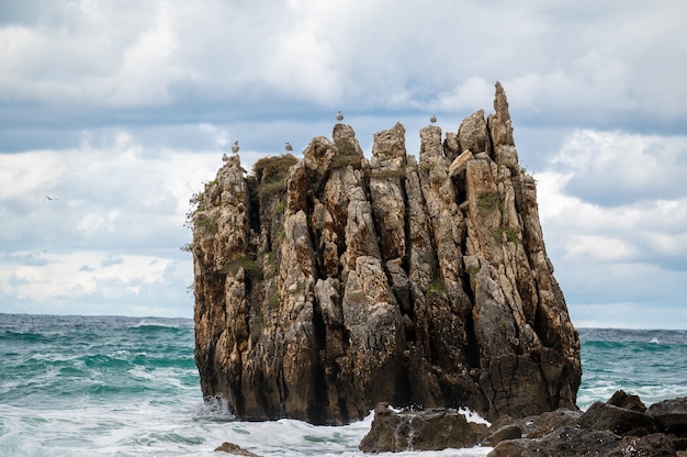 Salpicaduras de agua del océano en la playa de rocas con hermoso cielo y nubes. Ola de mar salpicando sobre piedra en la orilla del mar en invierno. Costa rocosa con aguas blancas arremolinándose alrededor de las rocas