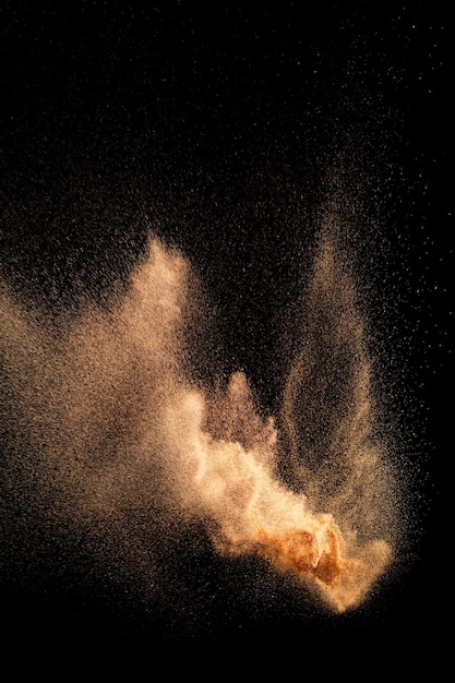 Foto salpicaduras de arena de color marrón sobre fondo negro onda de mosca de arena en el aire.