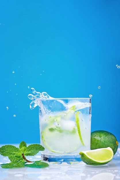 Salpicaduras de cóctel mojito con limón y menta fresca en vidrio sobre un fondo azul