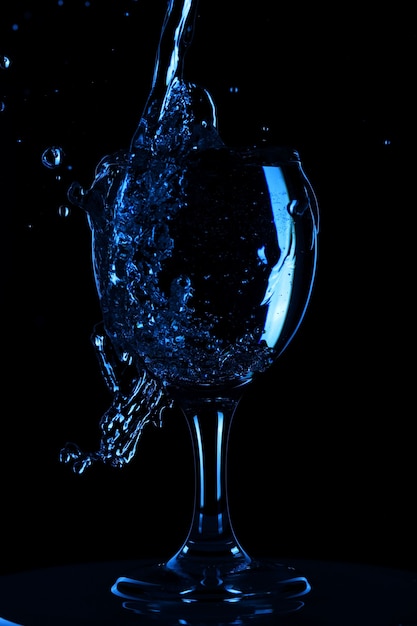 Las salpicaduras y las gotas de agua en un vaso se aíslan sobre un fondo negro. Agua azul en un vaso