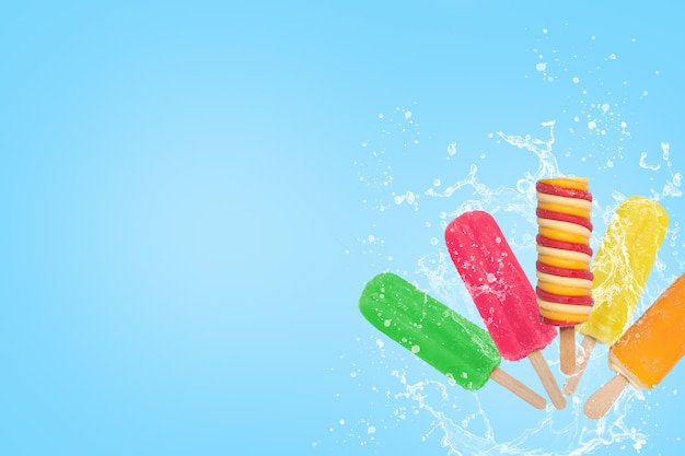 Salpicaduras de helado de paletas de colores sobre fondo azul con espacio de copia.