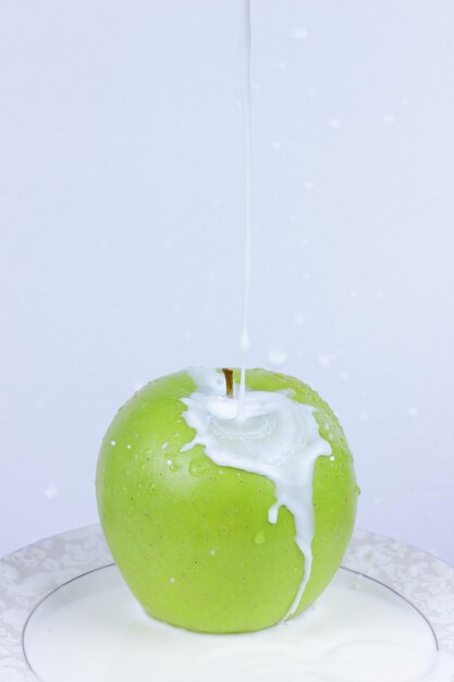 Salpicaduras de leche con una manzana en un plato blanco. Manzana verde con leche vertida