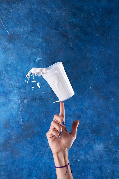 Salpicaduras de leche en un vaso de levitación sobre un fondo azul con una mano.