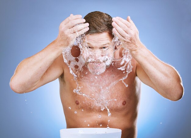 Foto salpicos de água do homem e higiene da pele por bacia para lavagem facial ou sustentabilidade natural contra fundo azul do estúdio lavagem masculina em tratamento facial por pia para bem-estar limpo ou autocuidado