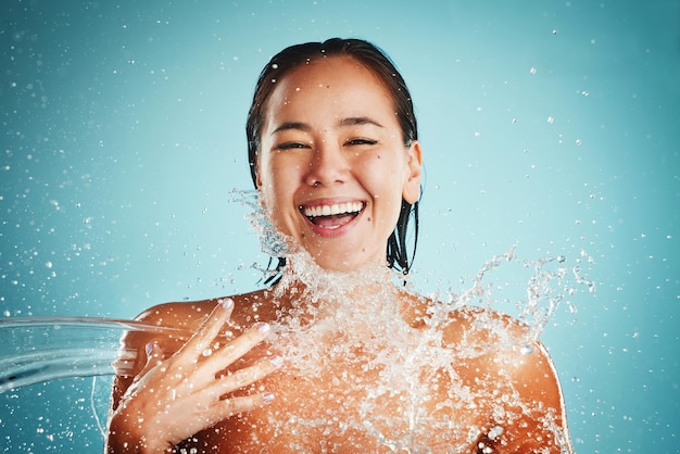 Foto salpicos de água felizes e mulher no estúdio para limpeza de cuidados com a pele e beleza em um fundo azul mock up modelo asiático de anúncio de respingos de beleza facial relaxe com produto de água e rosto de pele e bem-estar