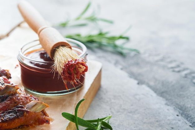 Salsa de barbacoa picante y picante en un recipiente de tarro con cepillo de hilvanado sobre fondo gris de piedra antigua Composición plana Concepto de comida americana Vista superior Espacio para texto