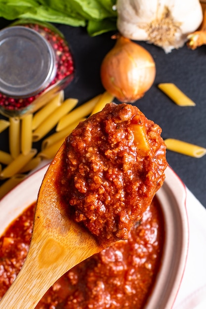 Salsa boloñesa casera de cocción lenta en maceta de cerámica roja y penne crudo