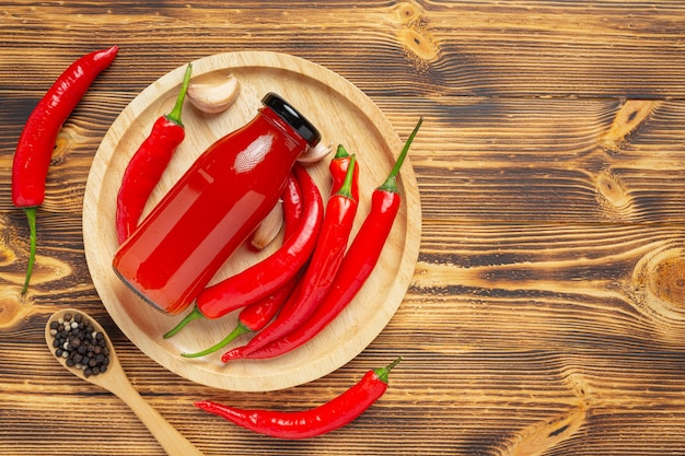 Salsa de Chile en botella y pimientos sobre superficie de madera