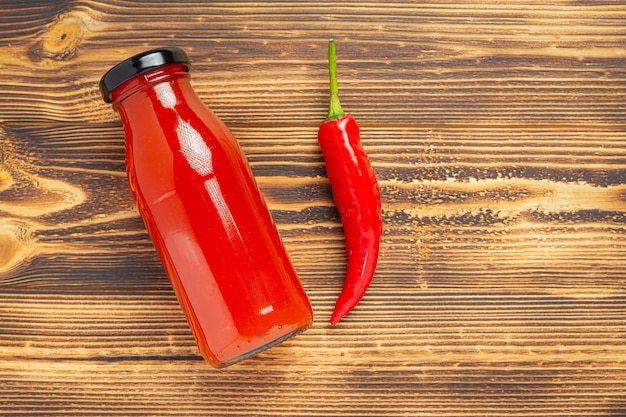 Salsa de Chile en botella y pimientos sobre superficie de madera