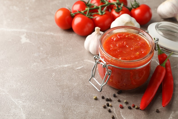 Salsa de chile en frasco de vidrio e ingredientes en gris, espacio para texto