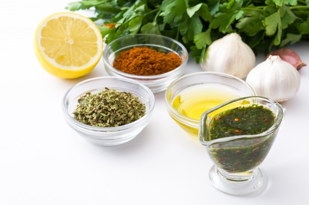 Salsa de chimichurri verde e ingredientes aislados en la superficie blanca