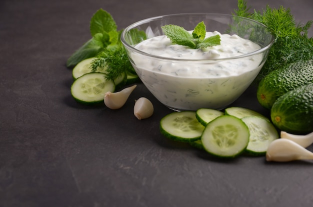 Salsa e ingredientes tzatziki. Salsa fresca del pepino y del eneldo en fondo oscuro.