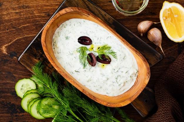 Salsa griega tradicional Tzatziki en cuenco de madera de olivo sobre fondo rústico antiguo