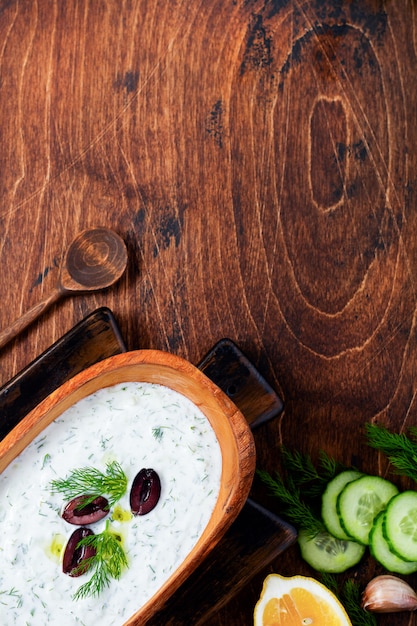 Salsa griega tradicional Tzatziki en cuenco de madera de olivo sobre fondo rústico antiguo