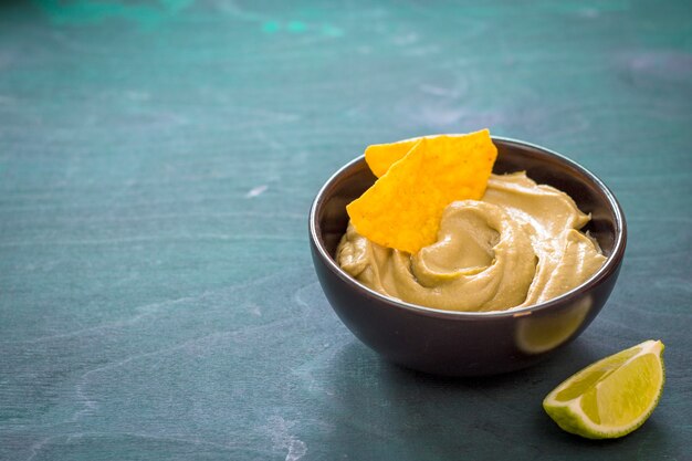 Salsa de guacamole mexicano en un bol con nachos crujientes sobre un fondo de madera. Espacio para texto. Salsa tradicional de aguacate.