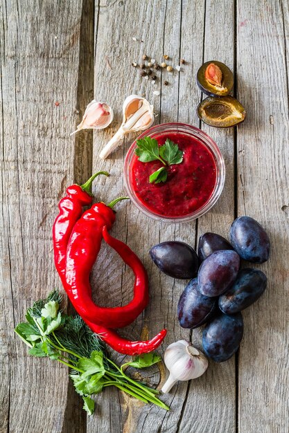 Foto salsa y ingredientes de tkemali sobre un fondo de madera rústica