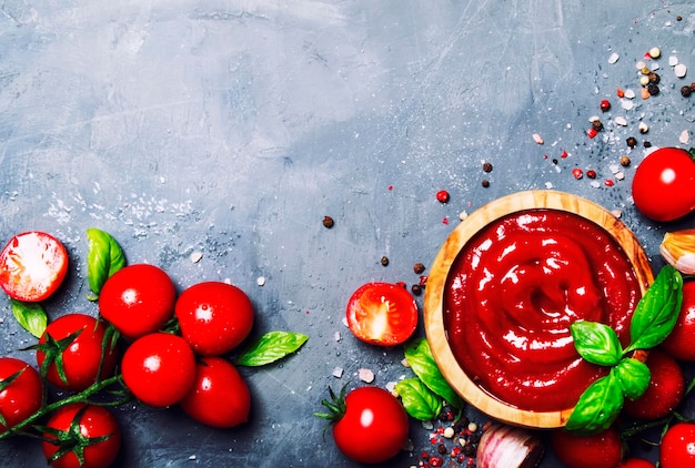 Salsa de ketchup de tomate caliente con especias de ajo y albahaca verde con tomates cherry en un tazón de madera sobre fondo de piedra gris vista superior