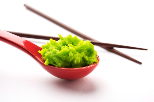 Salsa o pasta de wasabi verde en un tazón, con palillos o una cuchara sobre un fondo de colores lisos. enfoque selectivo