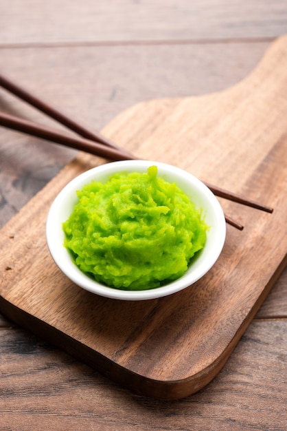 Salsa o pasta de wasabi verde en un tazón, con palillos o una cuchara sobre un fondo de colores lisos. enfoque selectivo