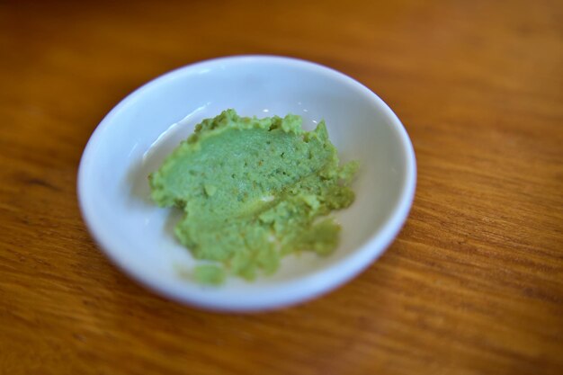 Foto salsa ou pasta de wasabi verde em uma tigela com pauzinhos ou colher sobre um fundo simples e colorido com foco seletivo