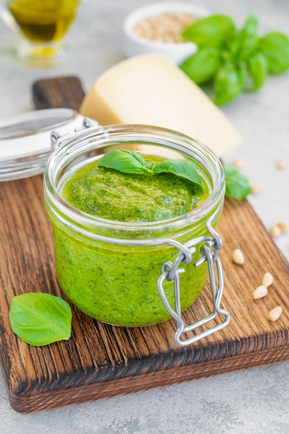 Salsa de pesto de albahaca italiana en un frasco de vidrio en una tabla con ingredientes para cocinar