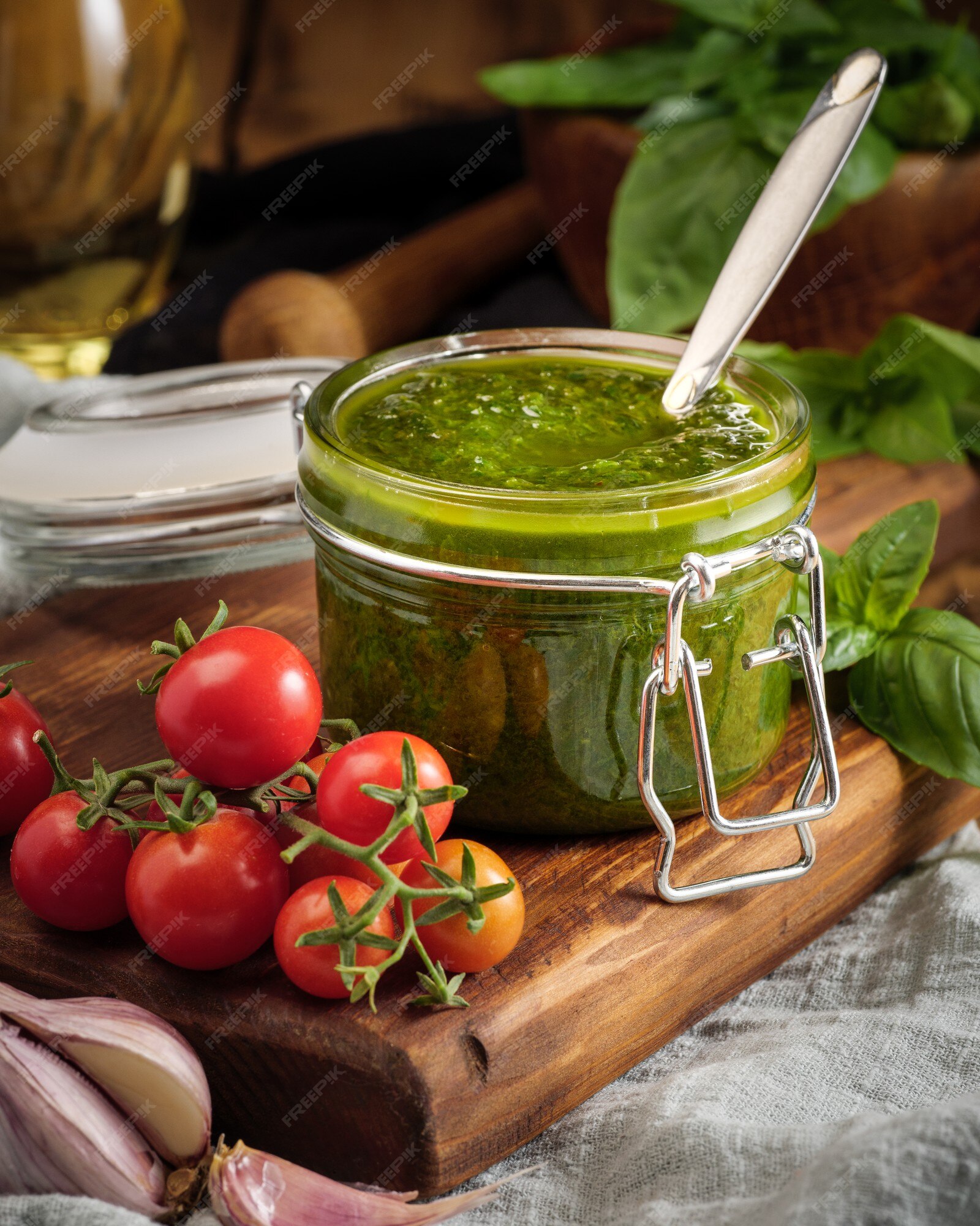 Salsa de pesto de albahaca italiana tradicional en un frasco de vidrio  sobre una tabla de madera junto con albahaca y tomates. | Foto Premium