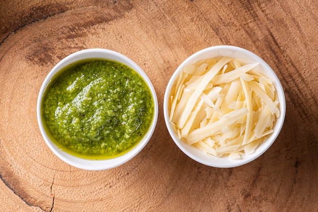 Foto salsa pesto en un bol con los ingredientes al fondo. aceite de oliva, ajo y albahaca.