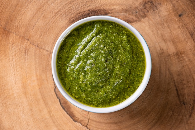 Foto salsa de pesto. en un vaso transparente con los ingredientes en la superficie. aceite de oliva, ajo y albahaca.