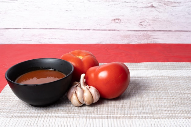 Foto salsa preparada en una olla negra e ingredientes para prepararla ajo y tomate