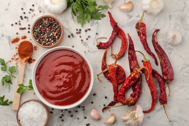 Foto salsa roja o salsa de tomate en un tazón e ingredientes para cocinar, especias, ajo, pimienta y hierbas.