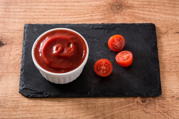 Salsa de salsa de tomate en un tazón y tomates en la mesa de madera