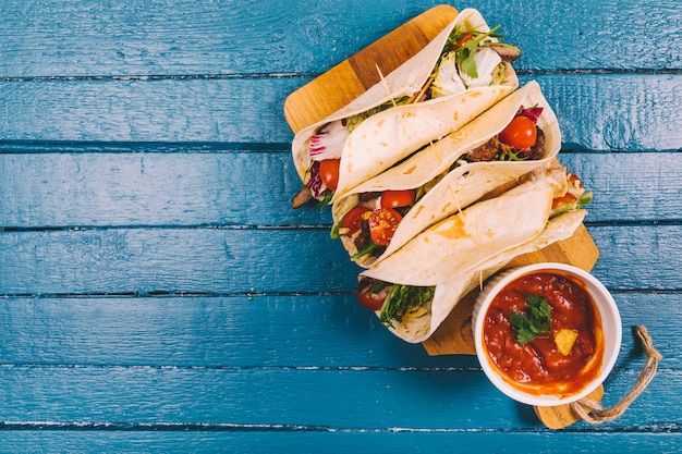 Foto salsa-sauce; mexikanische tacos mit fleisch und gemüse auf schneidebrett über blauem holzbrett