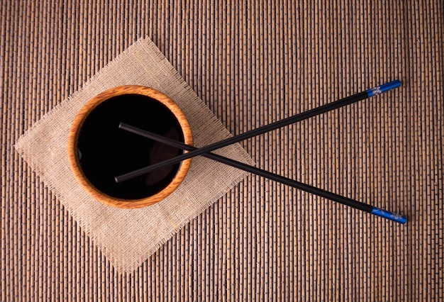 Salsa de soja y palillos en una estera de bambú, vista superior.