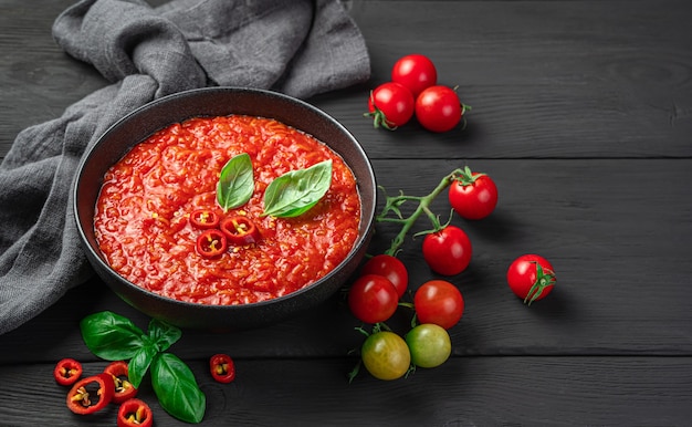 Salsa de tomate casera con albahaca sobre fondo negro. Vista lateral, espacio de copia