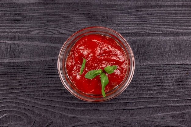 Salsa de tomate casera en un recipiente de vidrio para servir decorado con verduras sobre una mesa rústica de madera negra. Vista superior.