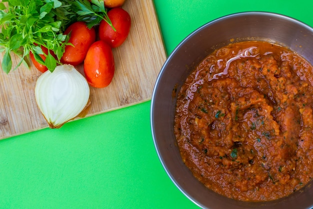 Foto salsa de tomate composición sobre fondo verde con tazón de salsa de tomate fresca los ingredientes tomate cebolla albahaca están en la tabla de madera