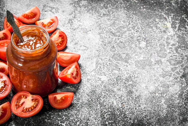 Salsa de tomate en frasco de vidrio con cuchara. Sobre fondo rústico.