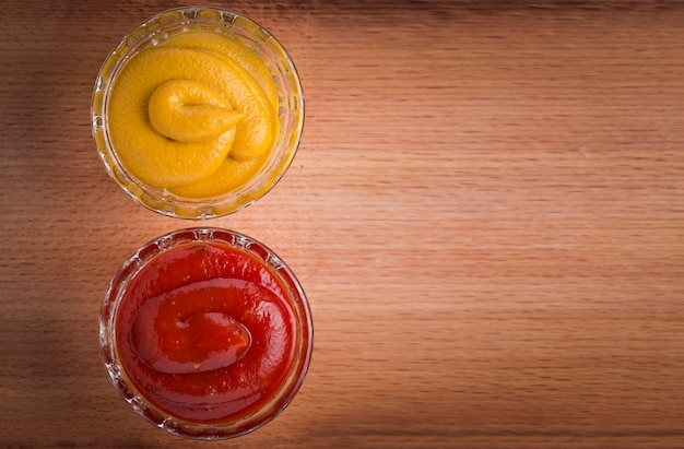 Salsa de tomate y mostaza en cuencos de cristal en la mesa de madera