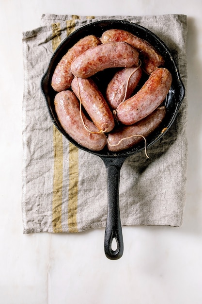 Salsiccia de salchichas italianas a la parrilla en sartén de hierro fundido sobre una servilleta de tela sobre fondo de mármol blanco. Endecha plana, espacio