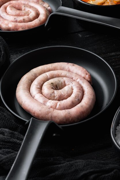 Salsicha crua em espiral numa frigideira de ferro fundido, no fundo preto da mesa de madeira