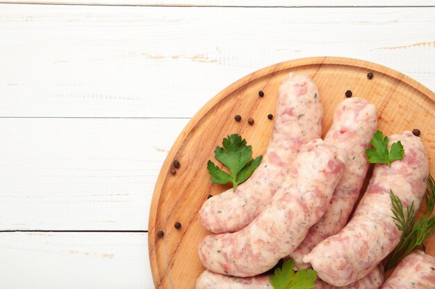 Salsicha crua na tábua de cortar na mesa de madeira branca