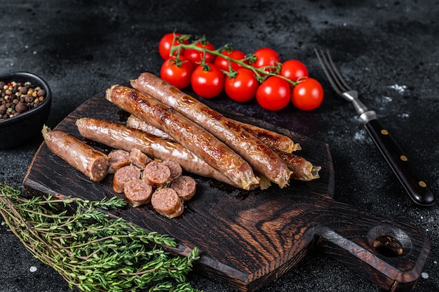 Salsicha de carne assada em uma placa de madeira com ervas e tomate. Fundo preto. Vista do topo.