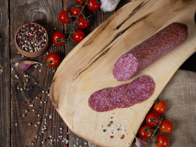Salsicha fatiada em uma placa de madeira com tomate de alho e pimenta Salsicha e especiarias em uma velha mesa de madeira