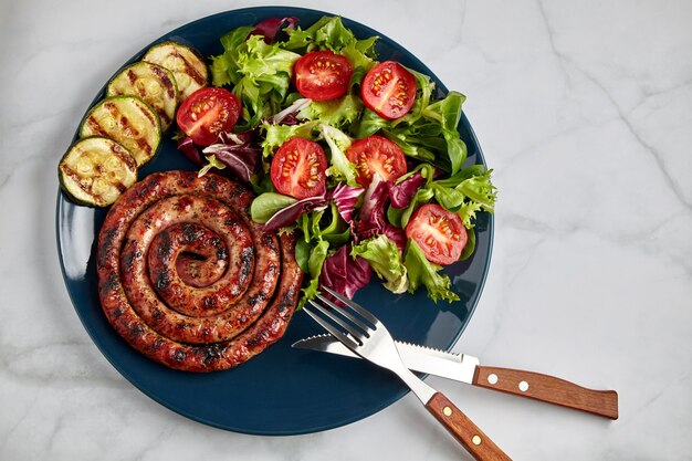 Salsicha grelhada em espiral com tomate e ervas em um prato azul