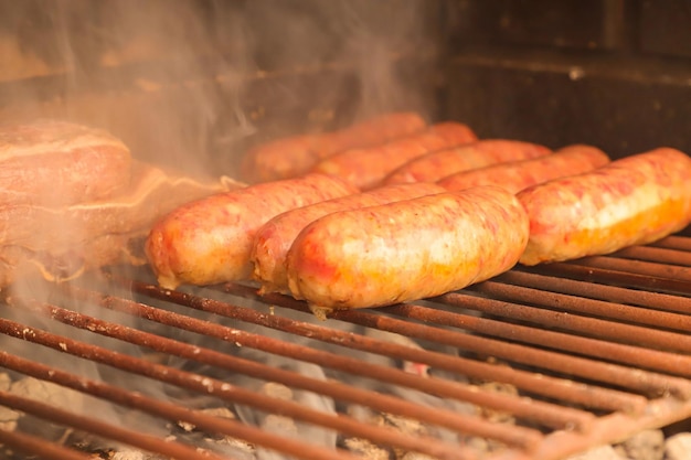 Salsichas cozinhando em uma grelha com fumaça saindo da grelha.