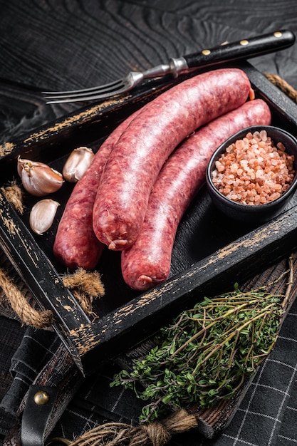 Salsichas cruas Bratwurst, carne fresca em bandeja de madeira com tomilho. Fundo de madeira. Vista do topo.