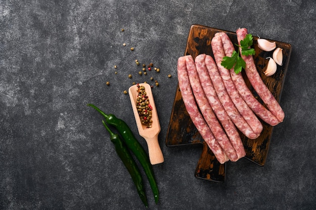 Salsichas cruas Bratwurst ou salsichas com ingredientes na tábua com especiarias em um fundo de pedra com espaço de cópia Fundo de cozimento de alimentos Vista superior