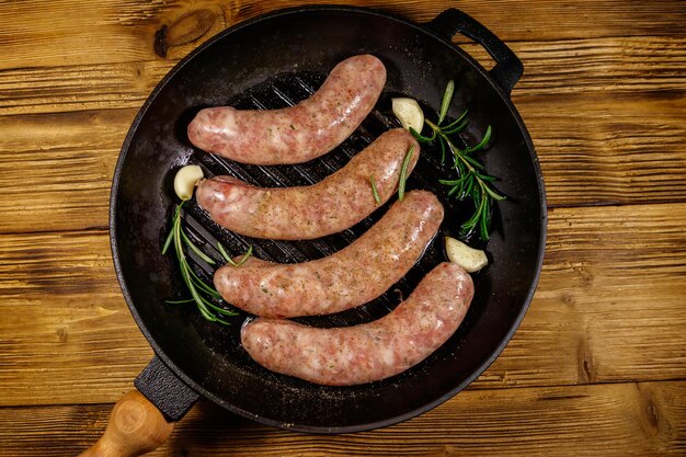 Salsichas cruas prontas para preparação com alho alecrim e especiarias em frigideira de grelha de ferro fundido na mesa de madeira Vista superior