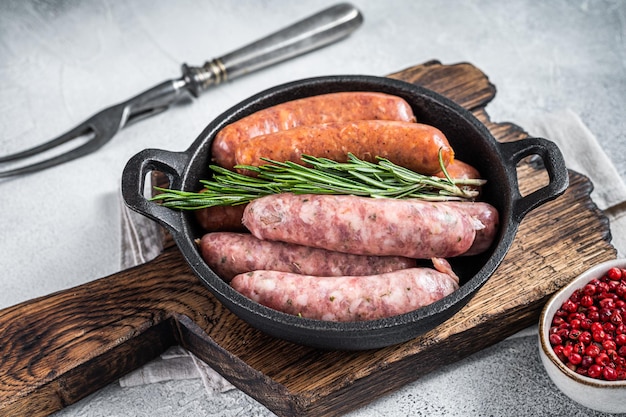 Salsichas crus sortidas chorizo e bratwurst com especiarias em uma panela com alecrim. fundo branco. vista do topo.