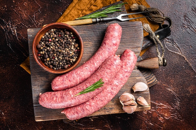 Salsichas de carne crua Bratwurst na placa de madeira com especiarias Fundo escuro Vista superior